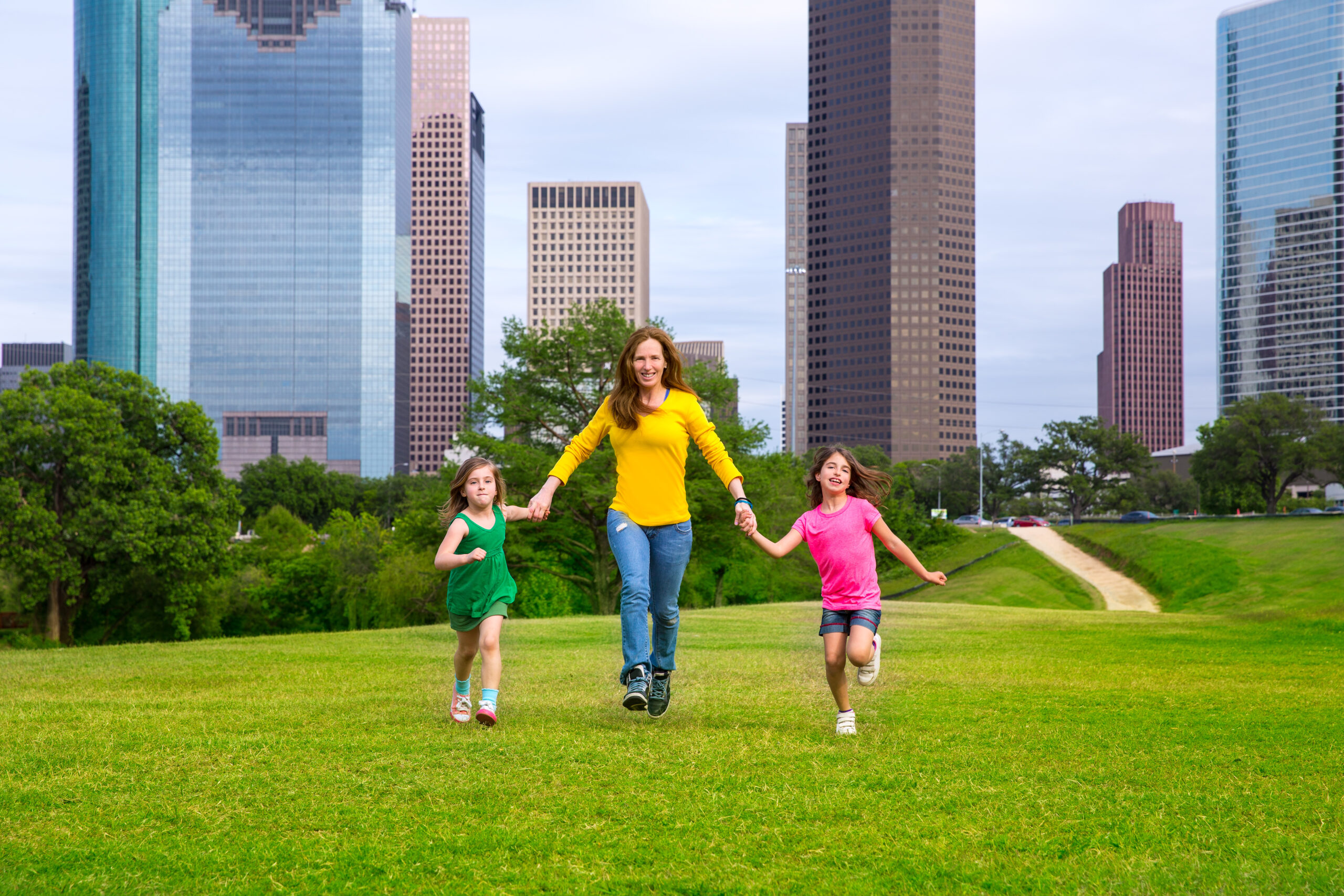 Mother and daughters walking holding hands on Houston skyline over park green lawn