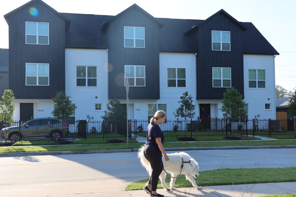 woman walking white dog in front of home Wycliffe neighborhood in Houston Texas